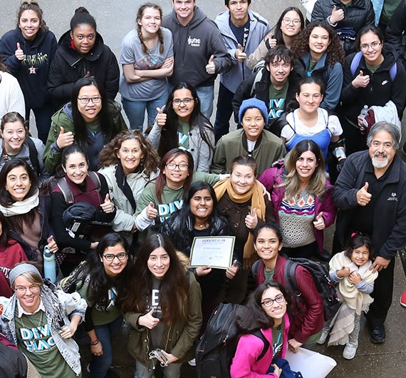 A diverse group of students, faculty and staff smile and give the gig 'em