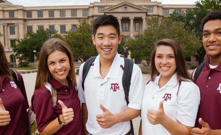 Five students give the gig'em in front of the Academic Building
