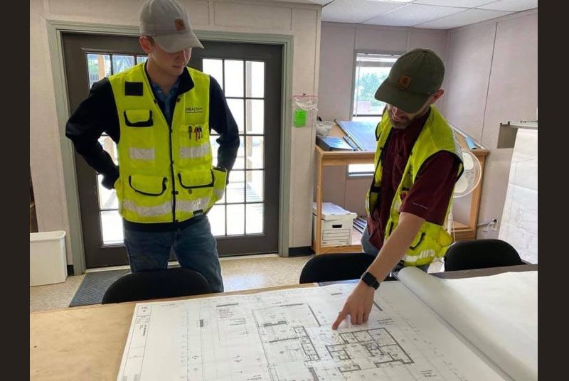 Two men wearing safety vests look at building plans