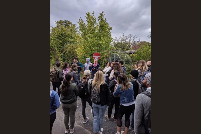 A tour guide instructs a group of students wearing jackets before they enter a garden