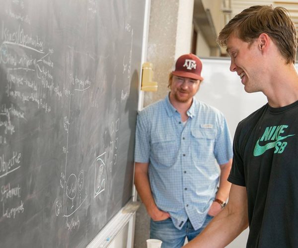 Two students smile while working at a classroom chalkboard