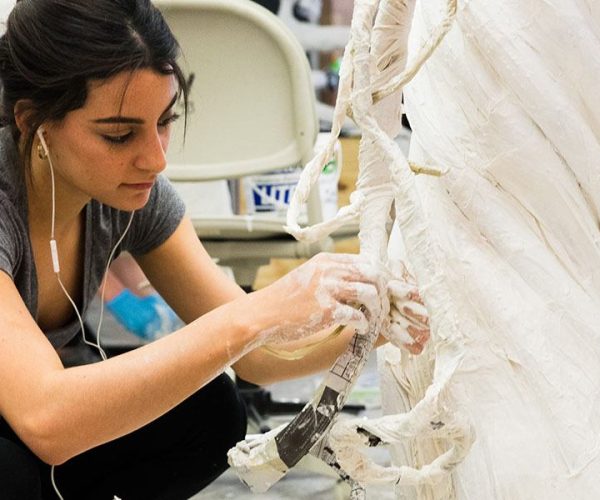 A student works on a paper mache sculpture in a studio