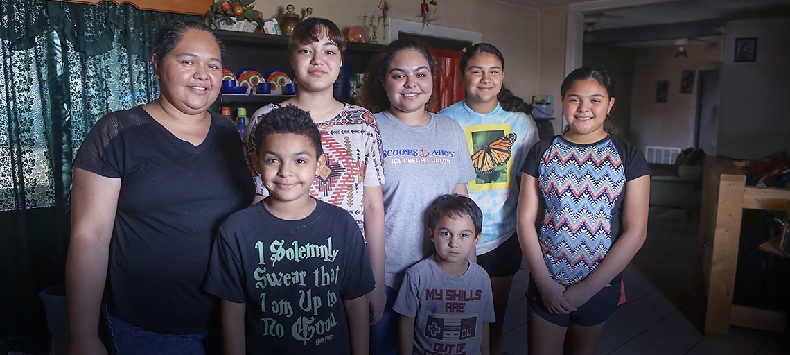 A family of seven smiles inside their home.