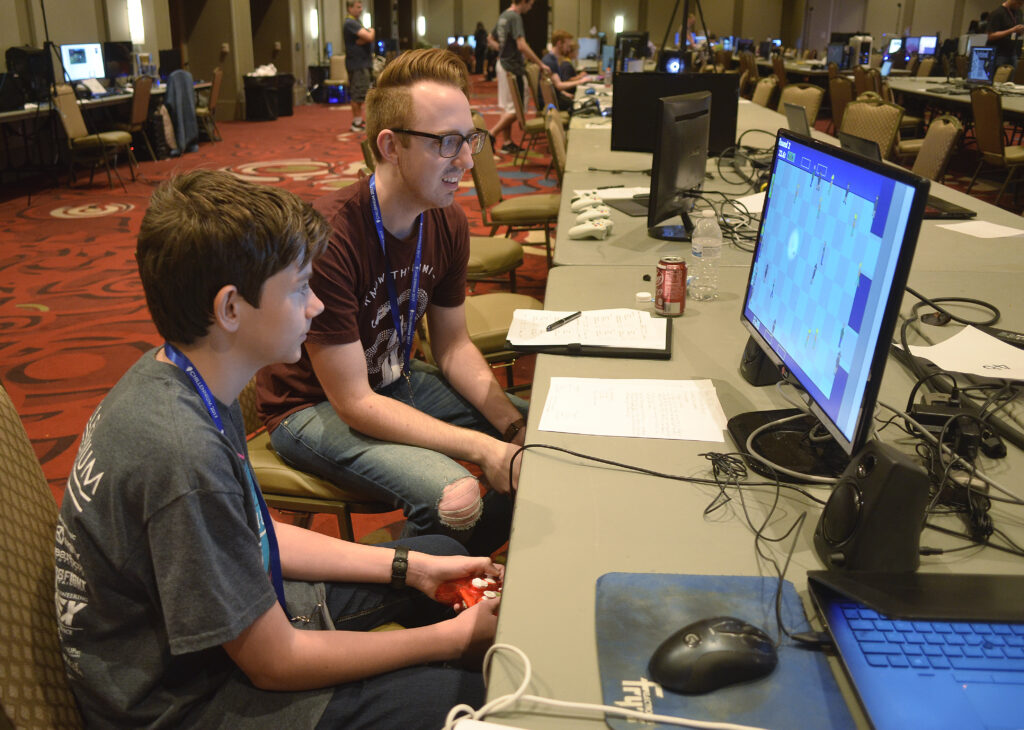 A young student and industry professional work on a computer together. 