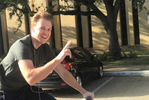 Cooper Goodman gives a peace sign while riding a bike on the Texas A&M campus