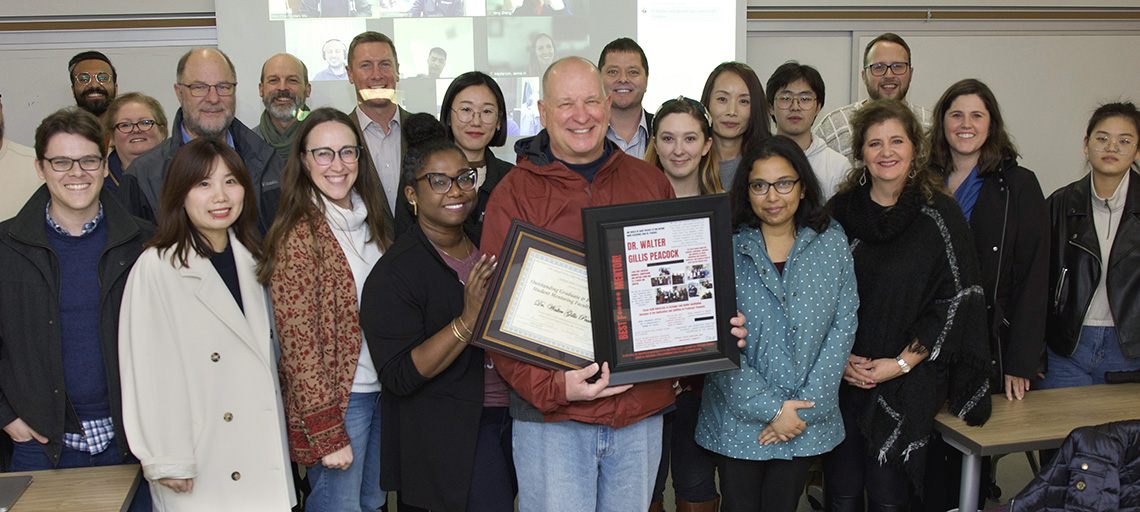 photo of Peacock holding awards, surrounded by faculty, students, and friends.