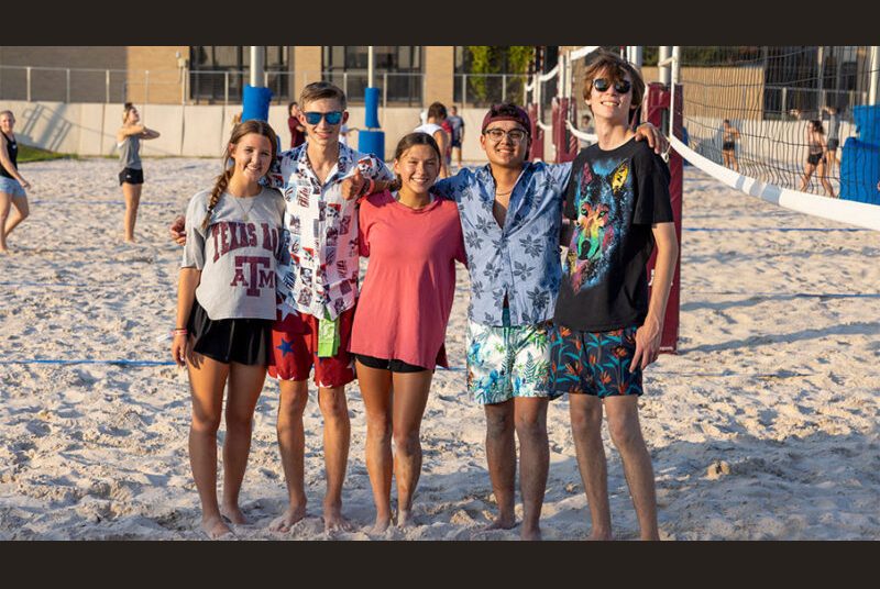 A group of Camp ARCH students pose on a sand volleyball court after playing a game