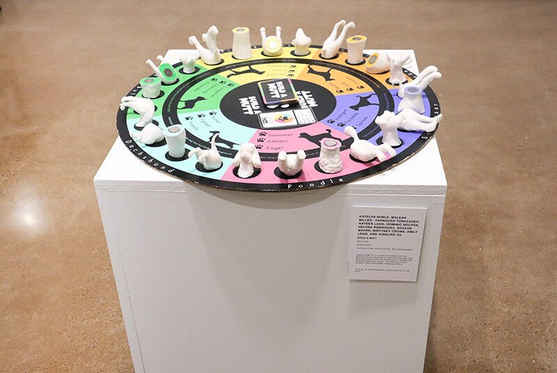 A close up photograph of a board game with various 3D printed dog parts, playing cards, and a colorful wheel with dog illustrations.
