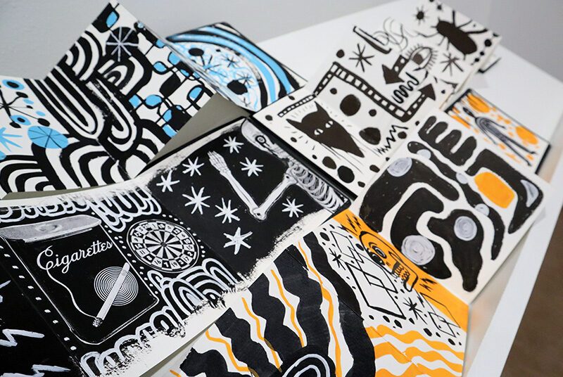 A close-up shot showing details of 3 accordion style sketchbooks featuring various sketches in black, white, blue and yellow.