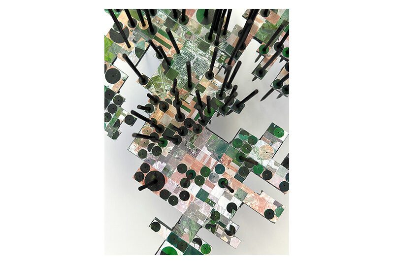A top down view of Lisa Woods’ sculpture showing the tops of the wooden sticks and a photograph printed on the foamcore. The photograph depicts an aerial view of various land use.