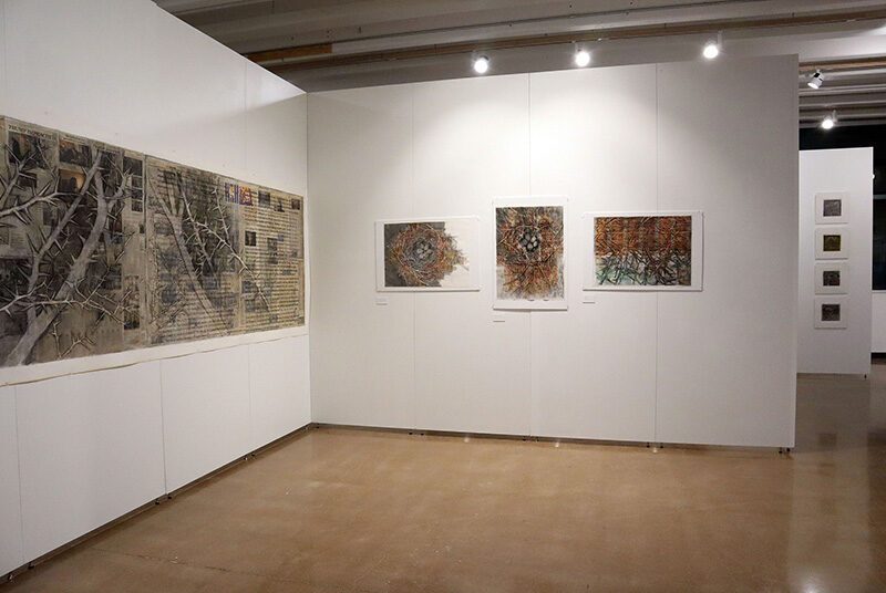 A view of one dark colored artwork on the left side that covers most of the gallery wall and 3 smaller artworks on the wall next to it featuring motifs of nests and thorns.