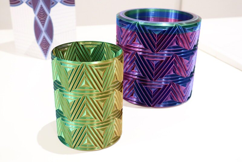 A close up view of 2 three-dimensional printed vases in green and purple iridescent filaments.