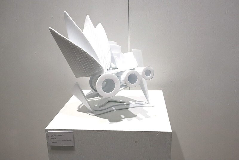 An organically shaped foam core sculpture with 3 cylinders and fin-like petals protruding at the top, sitting on top of a white pedestal.