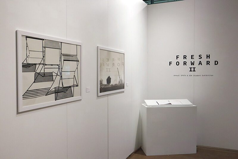 A view of two photographs next to the title of the student exhibition and a white pedestal. On the left, there is a black and white photograph of 3 wire chairs with their shadows. On the right, there is a photograph of an open field with a structure on the left side of the image.