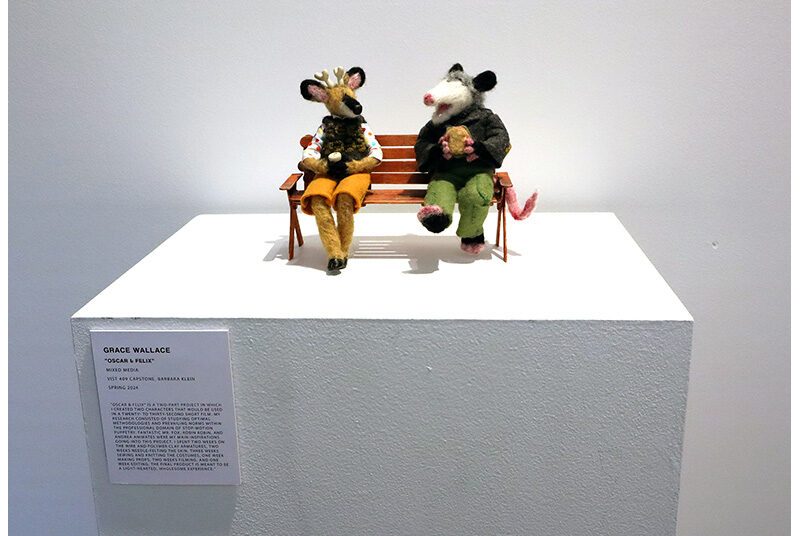 A view of 2 needle felted puppets sitting together on a bench enjoying snacks.