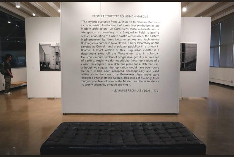 A black bench in front of an excerpt from the 1972 book “Learning from Las Vegas” in black vinyl on a white wall.