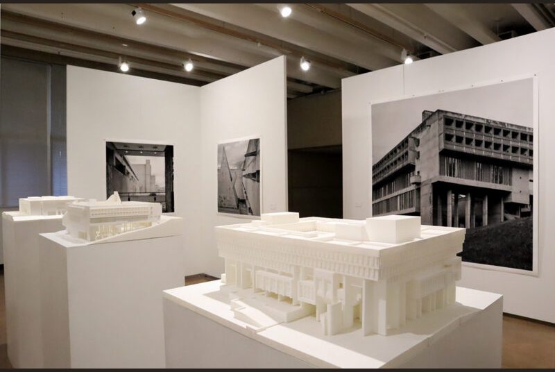 Three pedestals with 3D-printed models 3D-printed model of Boston City Hall on a white pillar with a very large print of Leonid Formansky’s “La Tourette Convent #0” behind it on a white wall.