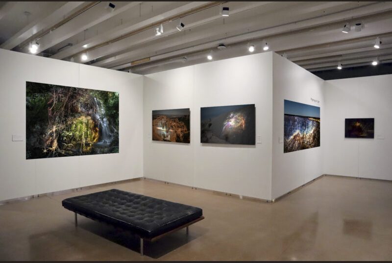 Large photographs are installed on a long white wall behind a black bench.