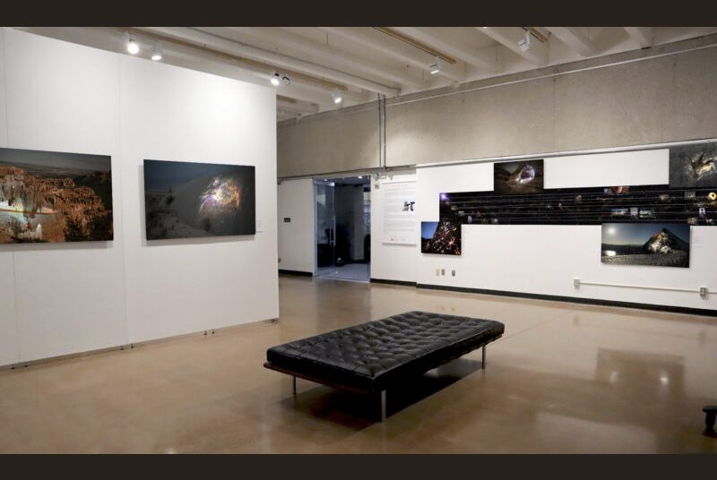Two large photographs are on the left. A black bench is in the center of the art gallery. On the right, beside the entrance doors there is a long horizontal artwork showing a timeline with 4 rectangular photographs attached below and above.