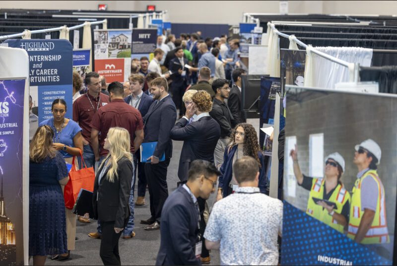 Crowds of students walk from booth to booth speaking to recruiters.