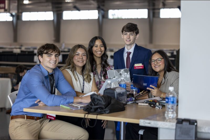A group of five professionally dressed students smile for a photo.