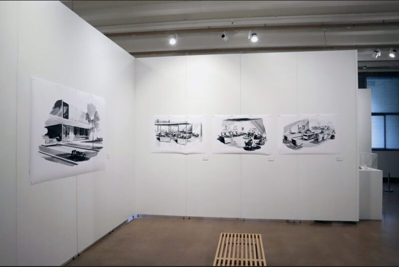 A large black and white painting of a bank on the left. In the center, 3 smaller paintings of the interior of the same bank are lined up. There is a wooden bench in the center of the gallery.