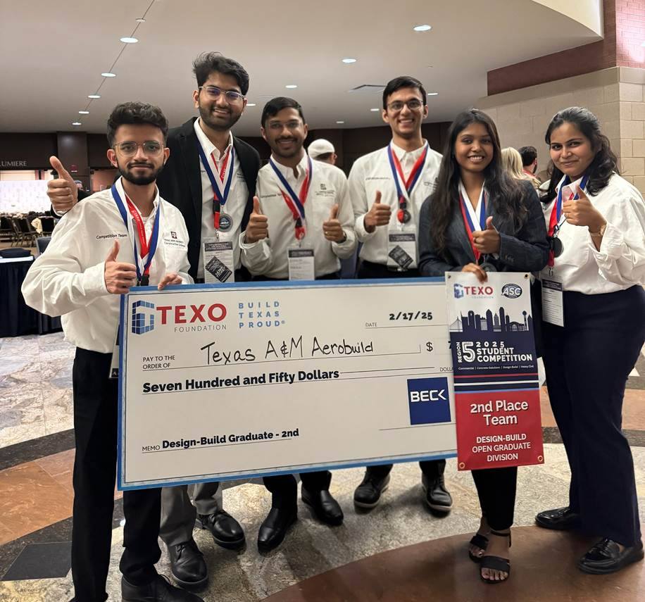 Six students holding a large check and wearing medals after winning a competition