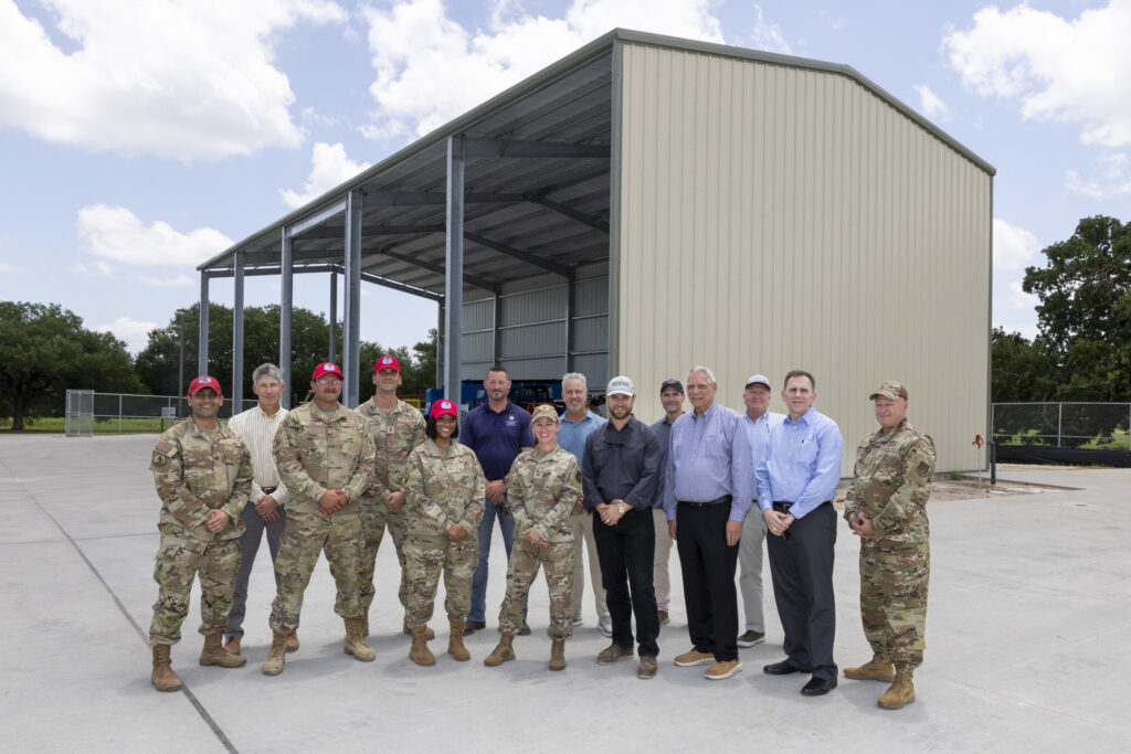 Fourteen people, including RED HORSE airmen and project donors, stand in front of the Construction Field Lab building on the Texas A&M-RELLIS campus.