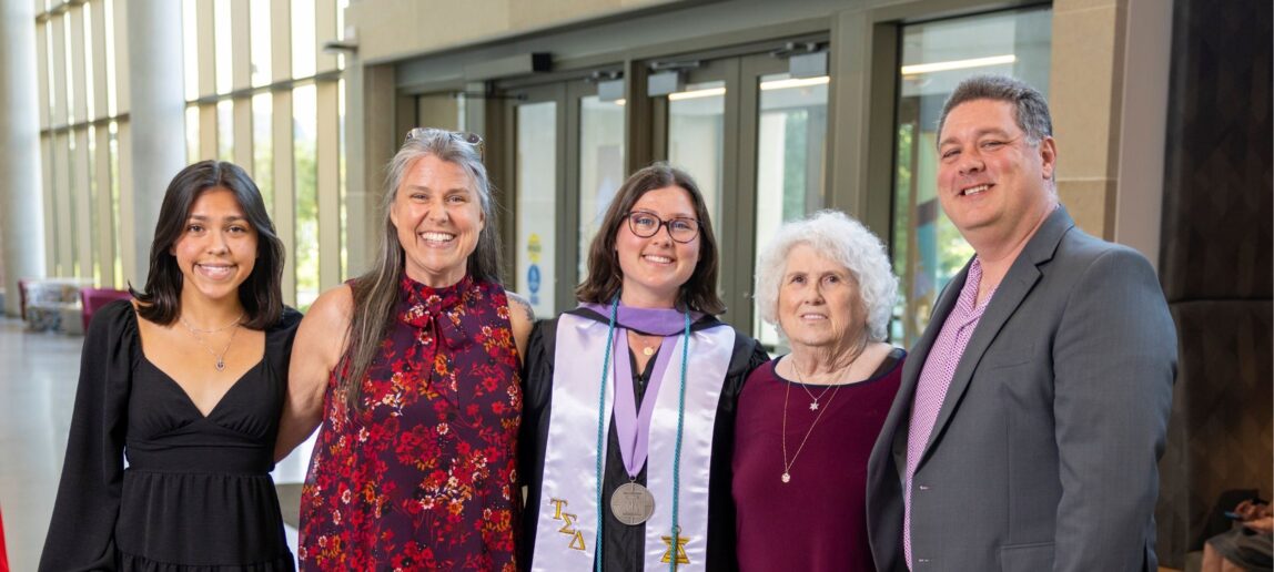 Emma Johnson smiles in her graduation regalia, surrounded by her family.
