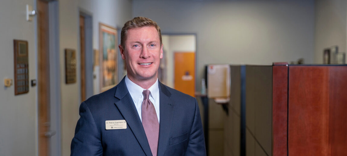 A man in a suit smiles in an office.
