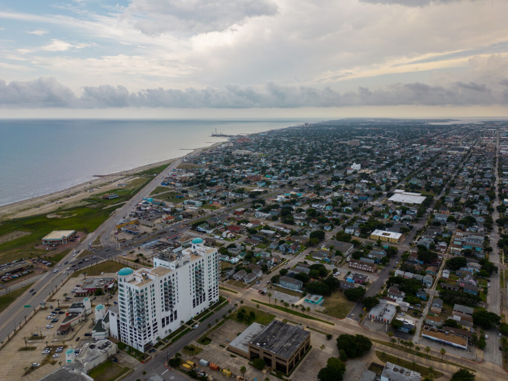 Aerial view of Galveston Beach with waves, shoreline, and nearby roads on a clear day.