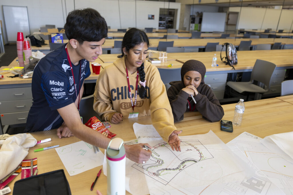 A male and a female student point to sections of a drawing while another female student watches.