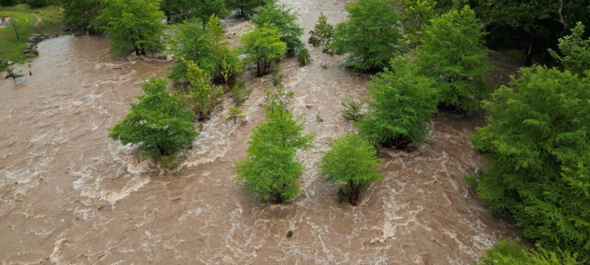 Aerial view of the flooded Guadalupe River flowing through the Texas Hill Country, with fast-moving rapids and surrounding vegetation partially submerged.