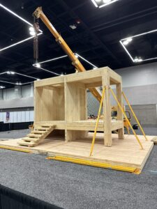 A completed live mass timber installation inside a convention center, featuring exposed glulam beams, CLT panels, and hardware connections under bright exhibit lighting.