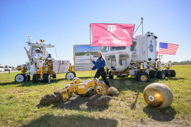 A woman plants a Texas A&M flag into the ground.