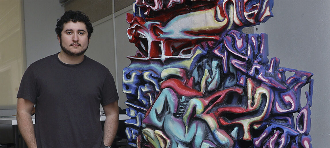 Student sculptor Quinn McCormack stands in front of his art installation